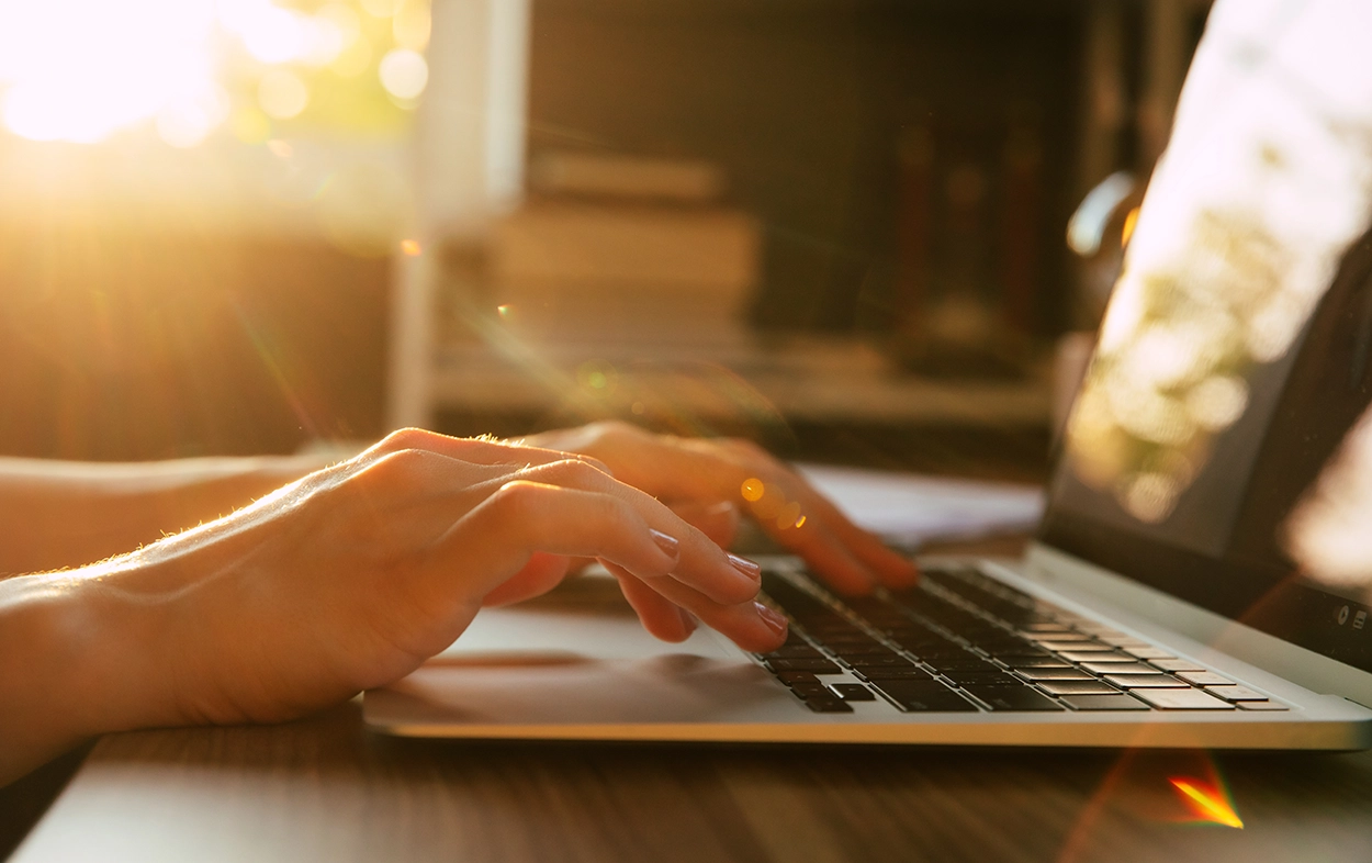 Handen op het toetsenbord van een laptop in warm avondlicht